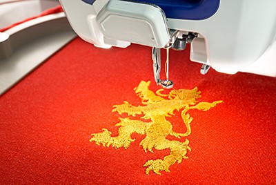 Embroidery machine and finish embroider gold lion design on red cotton fabric shirt, close up picture, copy space on the left side.